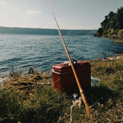 A fishing pole leaning on a red tackle box beside a lake
