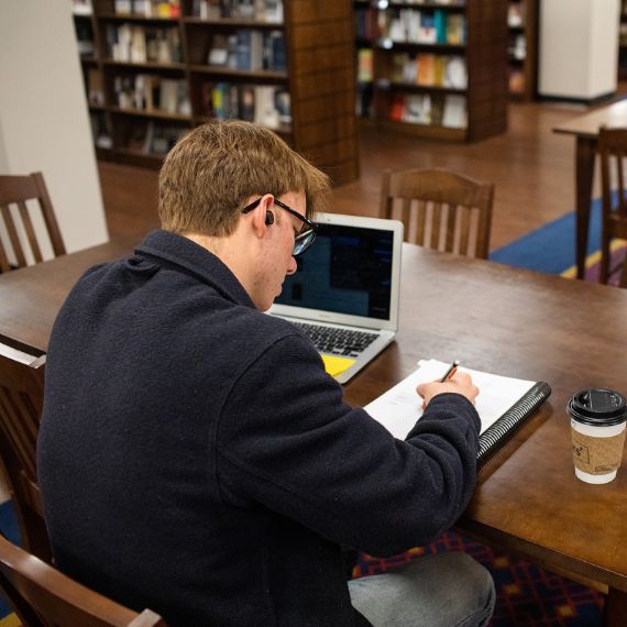 Male sbts student with laptop and coffee studying in bookstore
