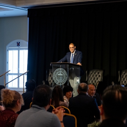 Dr. Carerra speaking at a lectern in front of a dark curtain backdrop